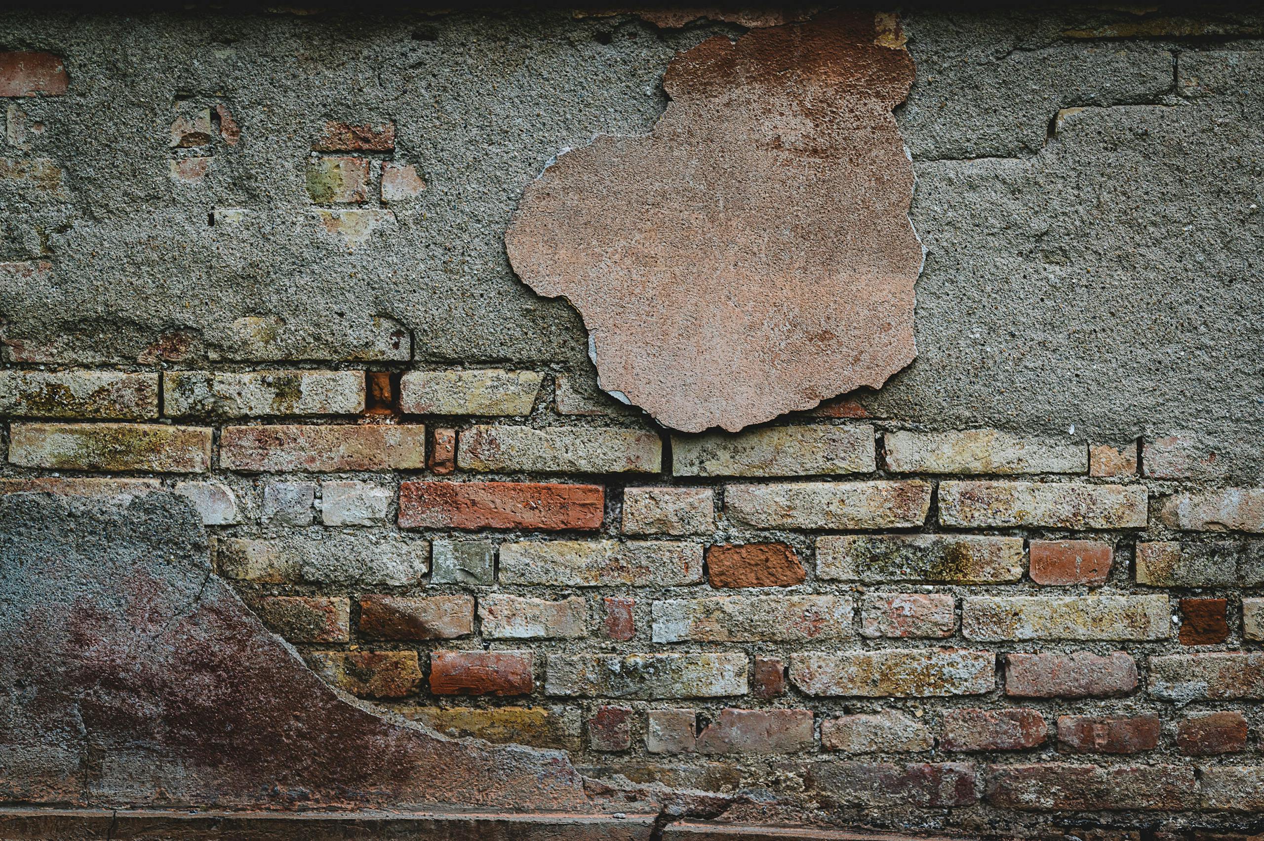 Close-up of a weathered brick wall with peeling plaster revealing rustic textures.