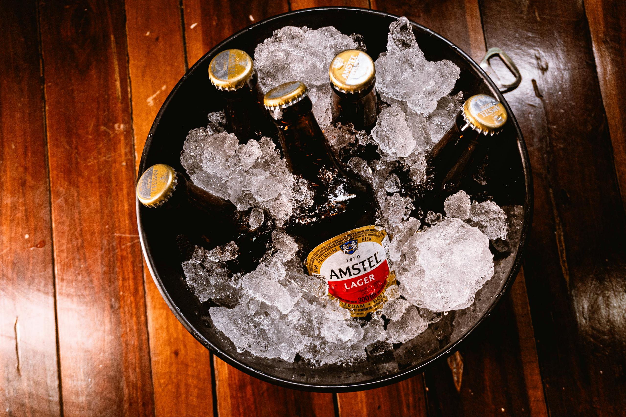 Close-up of Amstel Lager bottles chilled in ice on a wooden floor.