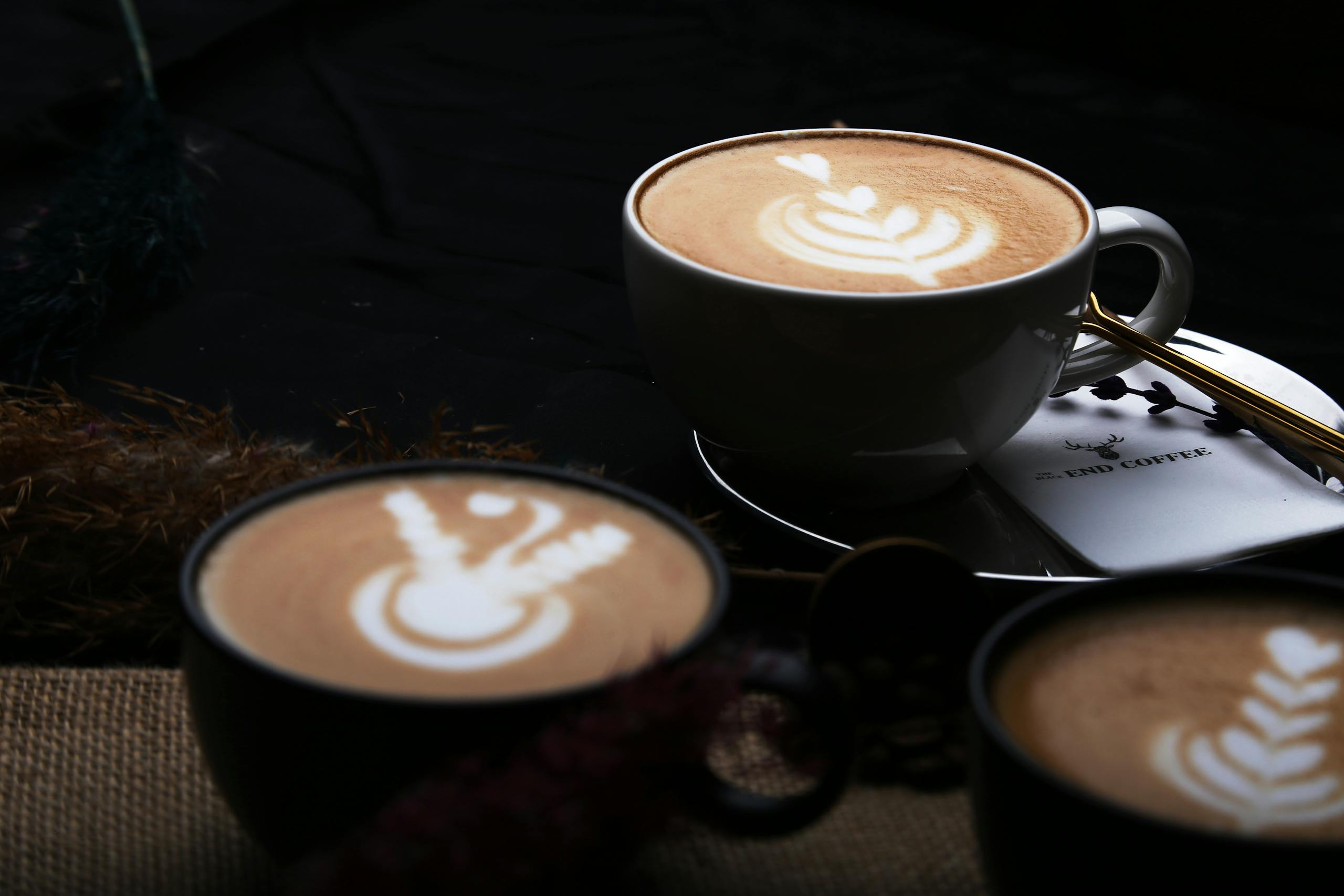 Close-up of beautifully crafted latte art in three cups of coffee, showcasing intricate designs.