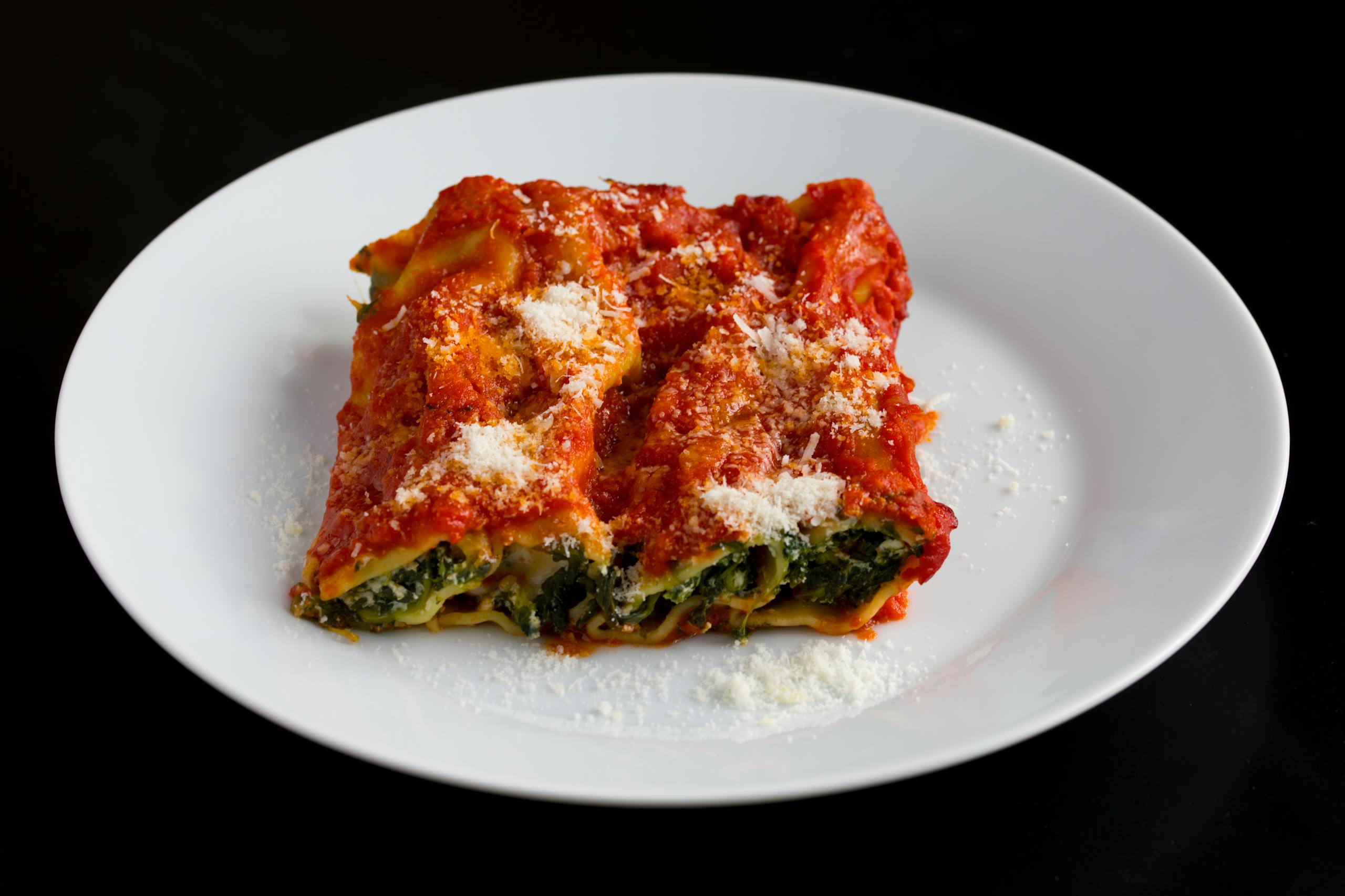 Close-up of classic spinach and ricotta lasagna topped with tomato sauce and parmesan on a white plate.