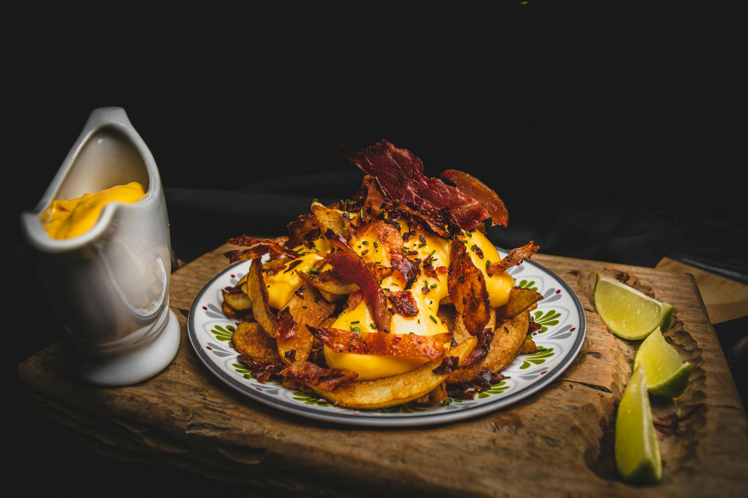Close-up of delicious potato chips topped with melted cheese and bacon, garnished with lime wedges.