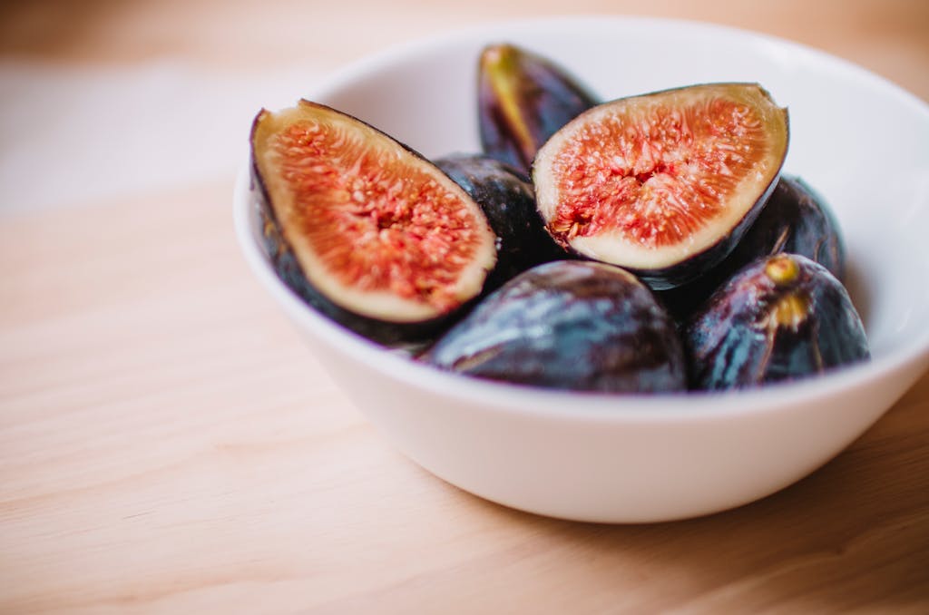 Close-up of fresh halved figs in a white bowl, showcasing their ripe texture and vibrant color.
