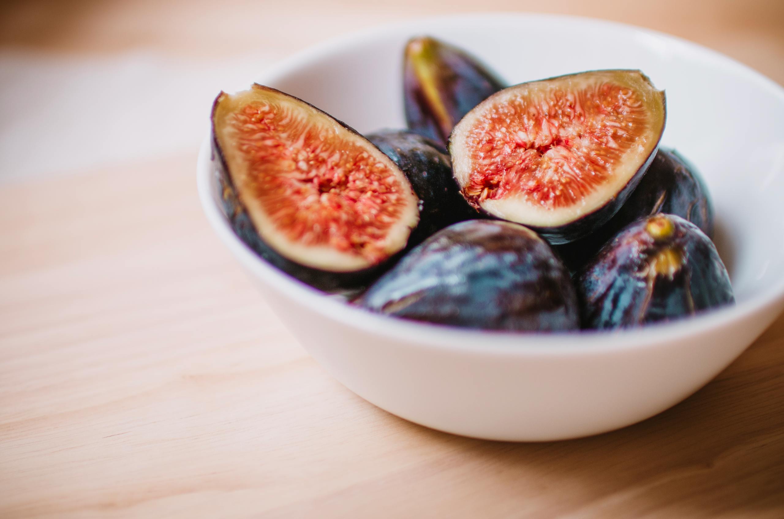 Close-up of fresh halved figs in a white bowl, showcasing their ripe texture and vibrant color.