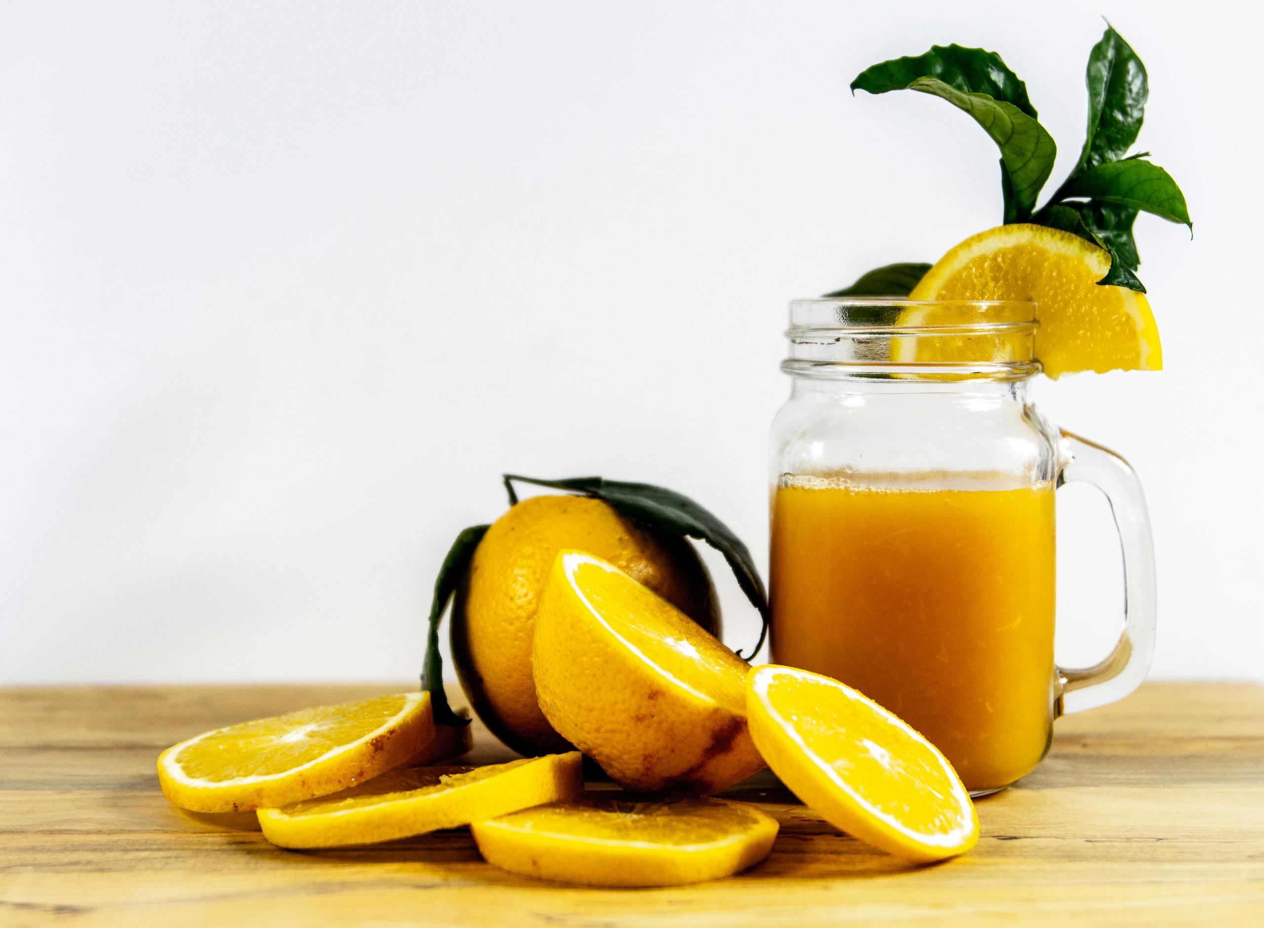 Close-up of fresh orange juice and sliced oranges in a mason jar on wooden table.