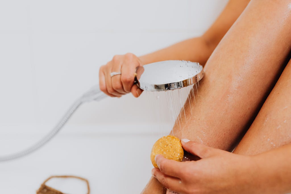 9 Bad Shower Habits You Need to Break Before It’s Too Late 1 Close-up of hands holding soap and shower head, highlighting skincare routine.