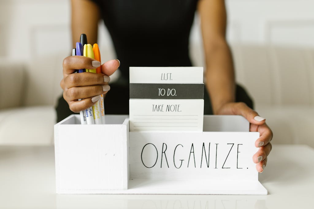 Close-up of hands organizing pens and notes in a white box labeled 'Organize.' Perfect for productivity inspiration.