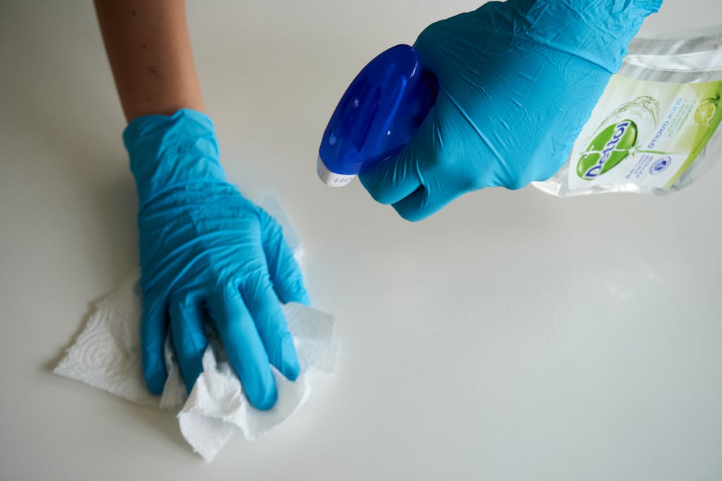 Close-up of hands wearing gloves cleaning a surface with disinfectant spray.