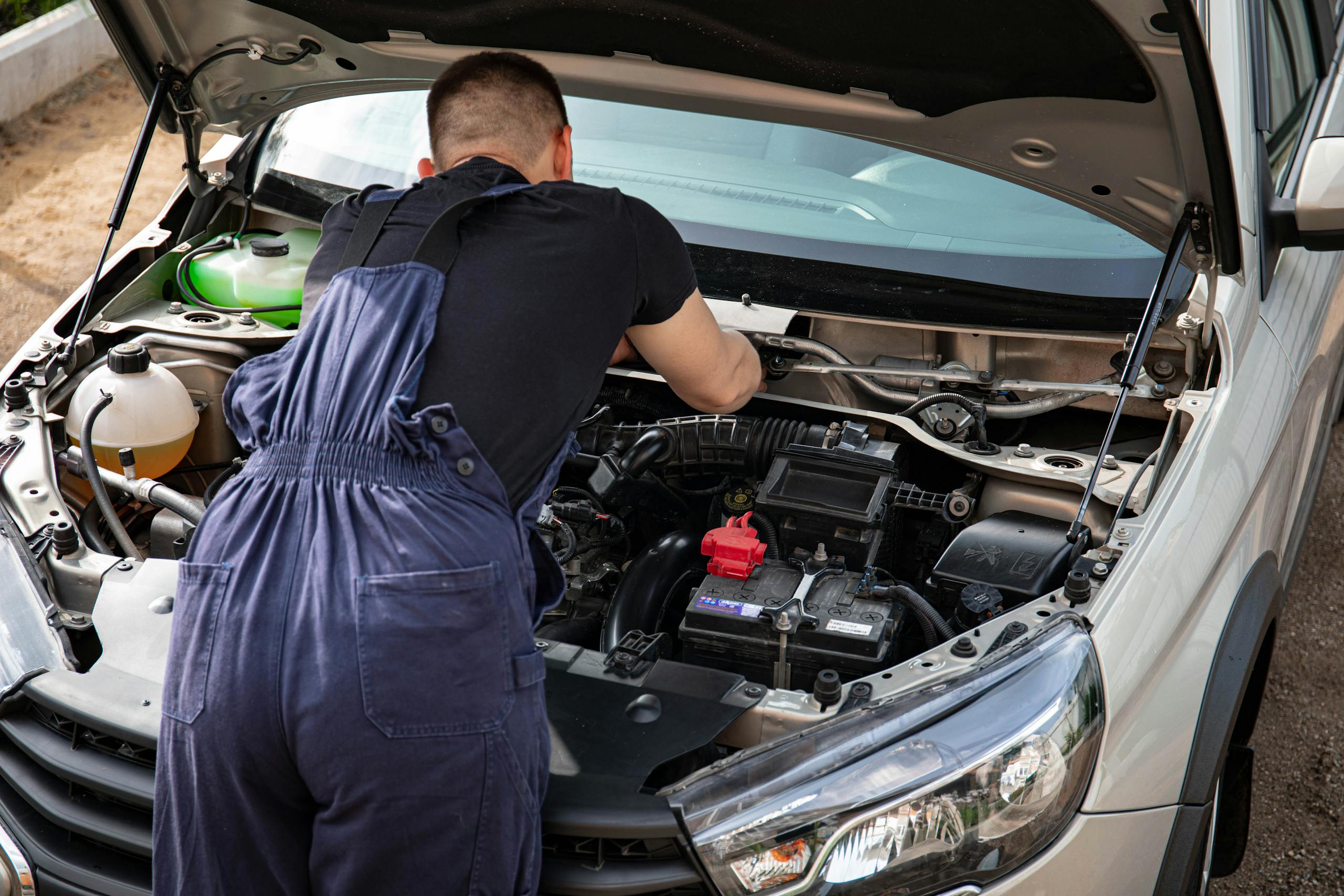 Close-up of mechanic repairing a car engine. Outdoor setting during the day.
