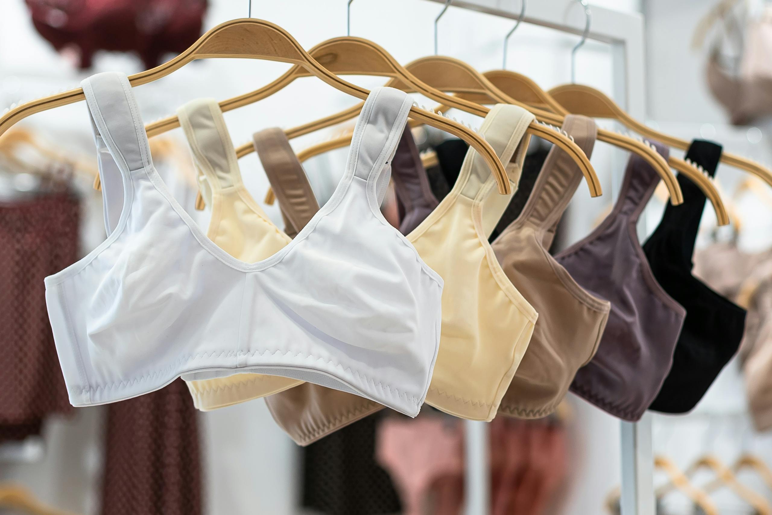 Close-up of sports bras in various colors displayed on wooden hangers in a fashion store.