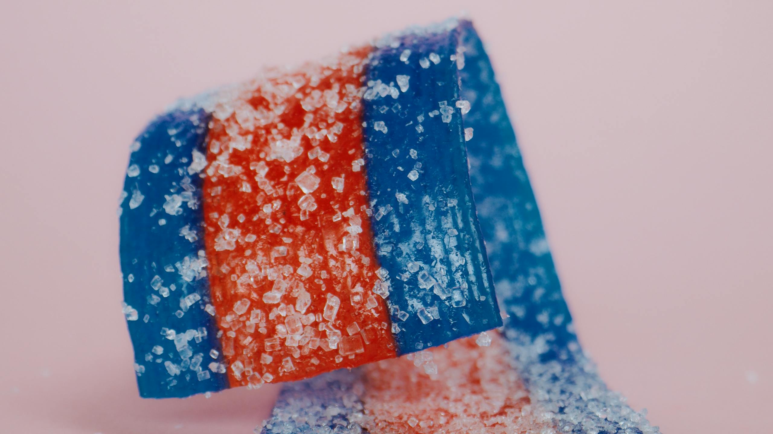 Close-up of vibrant red and blue sugared candy strips on a pink background, highlighting their texture.