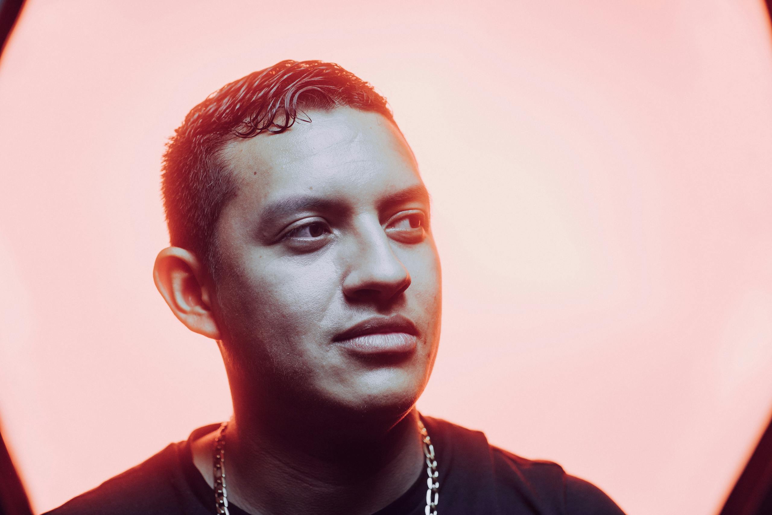 Close-up portrait of a young man with a stylish necklace against a pink background, emphasizing modern fashion.