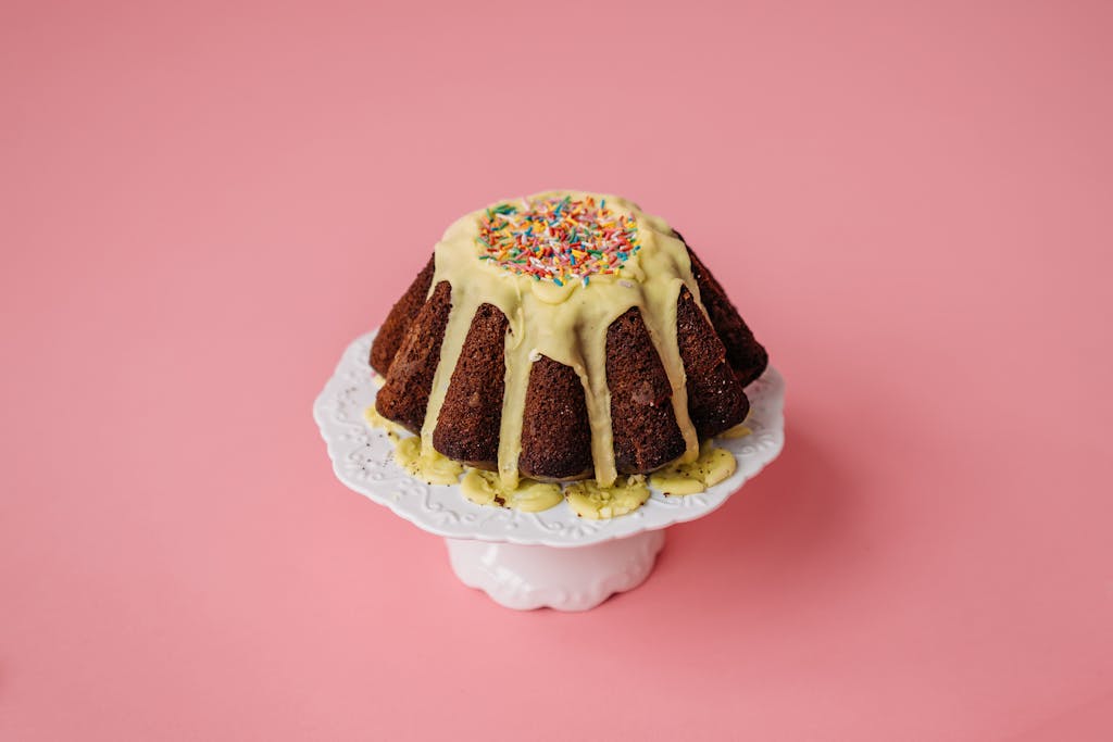 These 8 Foods Before Bed Are a Dangerous Mistake You Might Be Making 3 Colorful bundt cake with icing and sprinkles on a cake stand, set against a pink background.