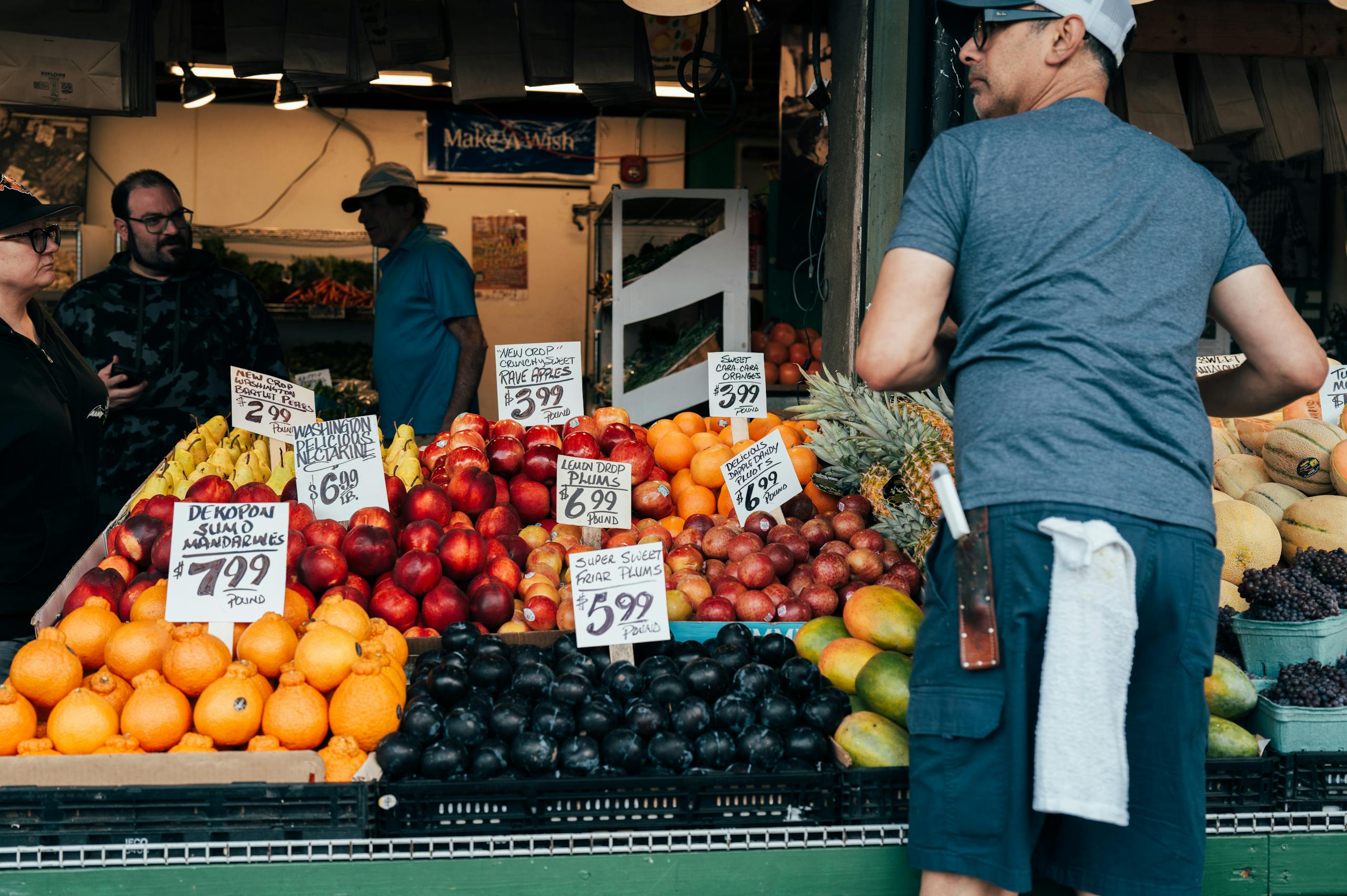 Colorful display of fruits at an outdoor farmers market stall with people shopping.