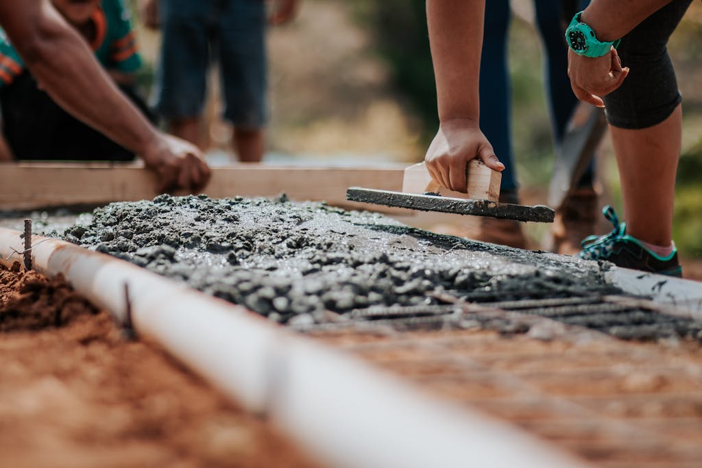 8 Repairs That Can Push You into Debt Before You Even Realize It 2 Construction workers leveling fresh cement on a sunny day at an outdoor site.