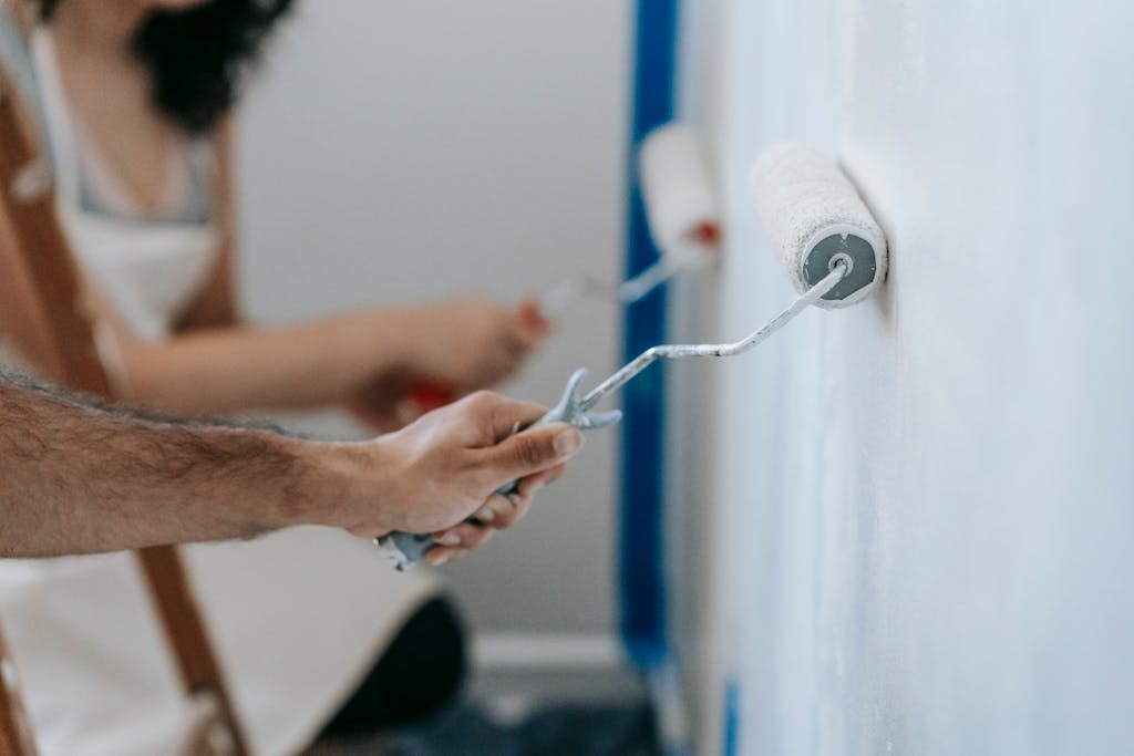 Your Home Looks Poor Because You Don't Know These 12 Decorating Tips 1 Couple painting a wall with rollers, perfect for home improvement and renovation themes.