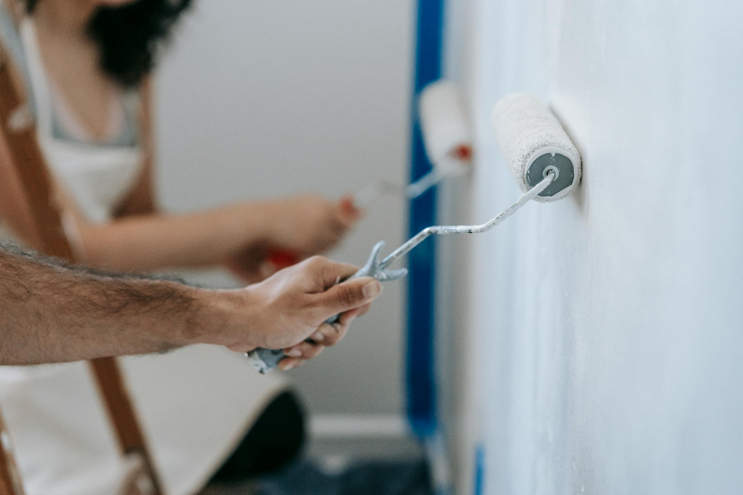 Couple painting a wall with rollers, perfect for home improvement and renovation themes.