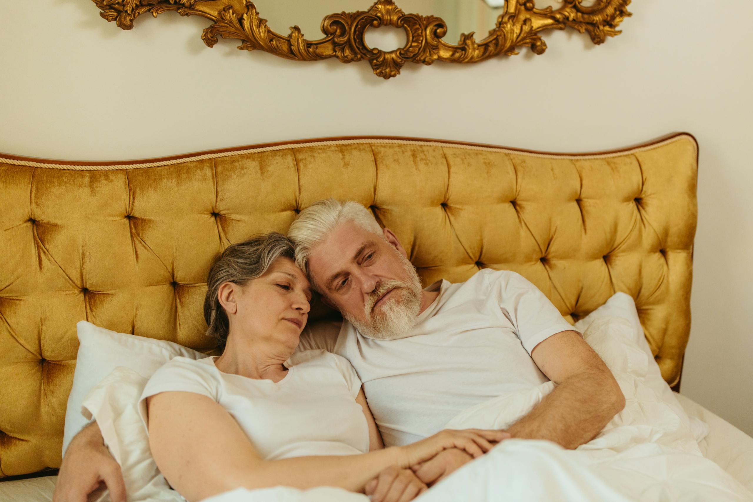 Cozy scene of an elderly couple resting in bed with a luxurious headboard.