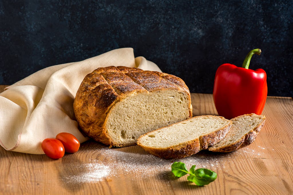 Delicious freshly baked sourdough bread with tomatoes and pepper on a rustic wooden table.