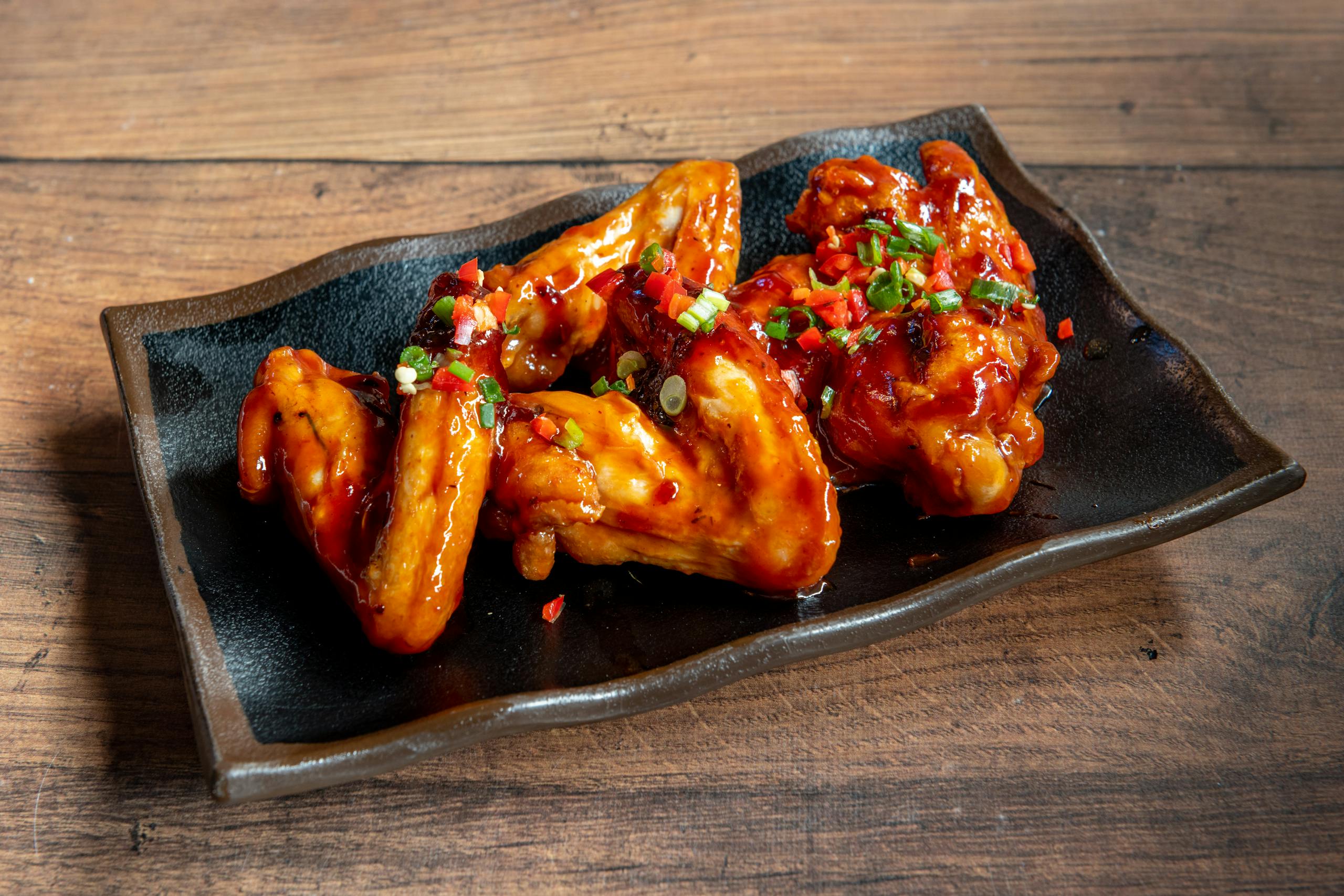Delicious glazed chicken wings served on a black plate, perfect for appetizers.