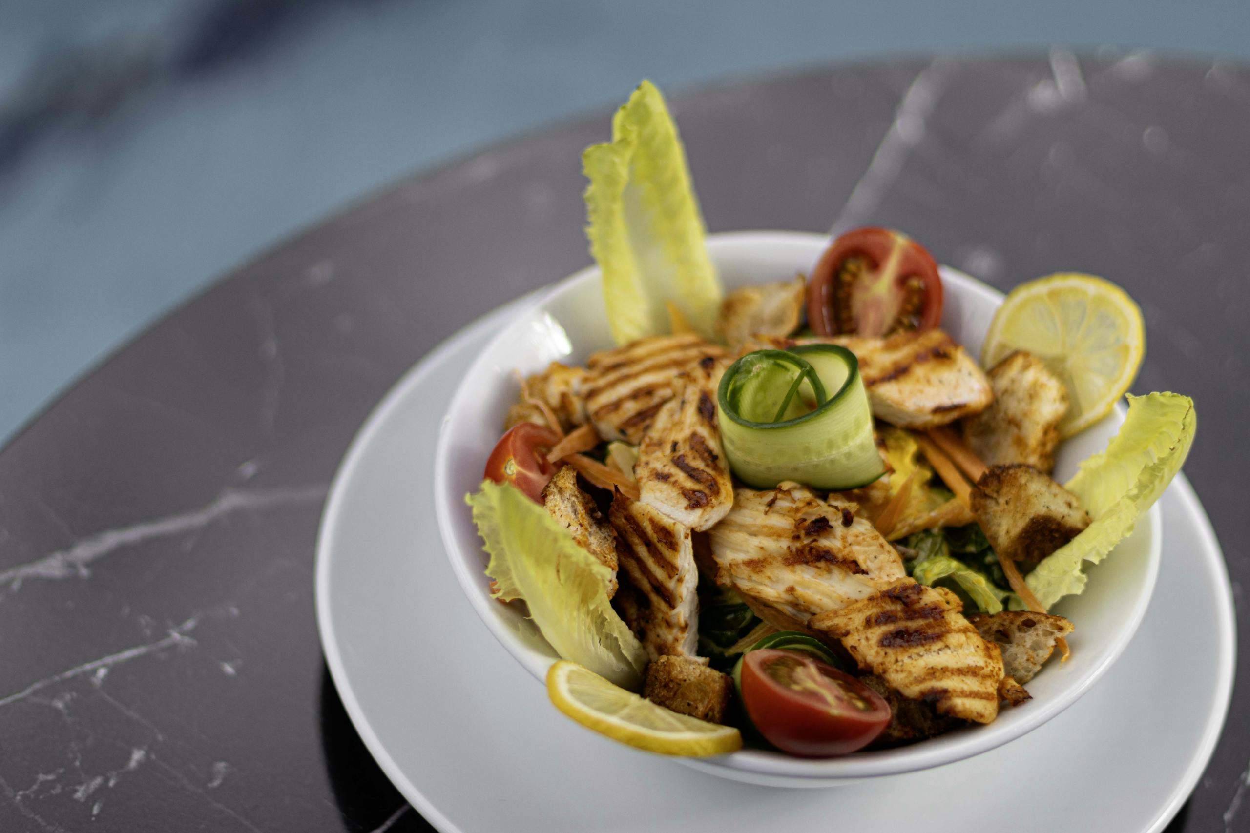 Delicious grilled chicken Caesar salad with fresh vegetables served on a marble table.