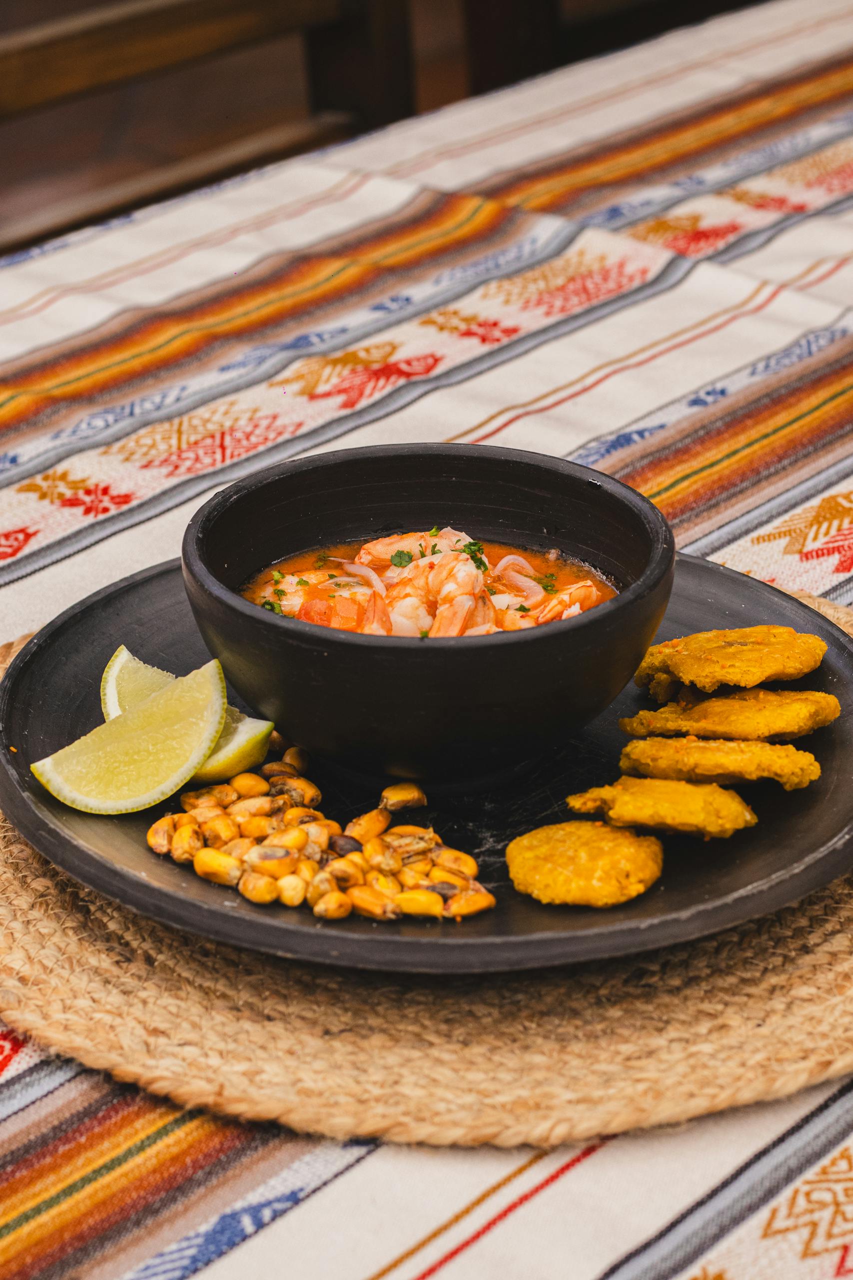 Delicious Latino shrimp ceviche served with lime, roasted corn, and plantain chips, on ethnic fabric.