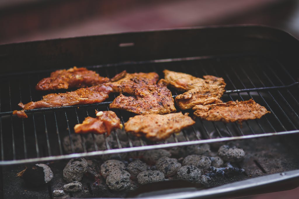 Delicious marinated meats sizzling on a charcoal barbecue grill, perfect for outdoor summer cooking.