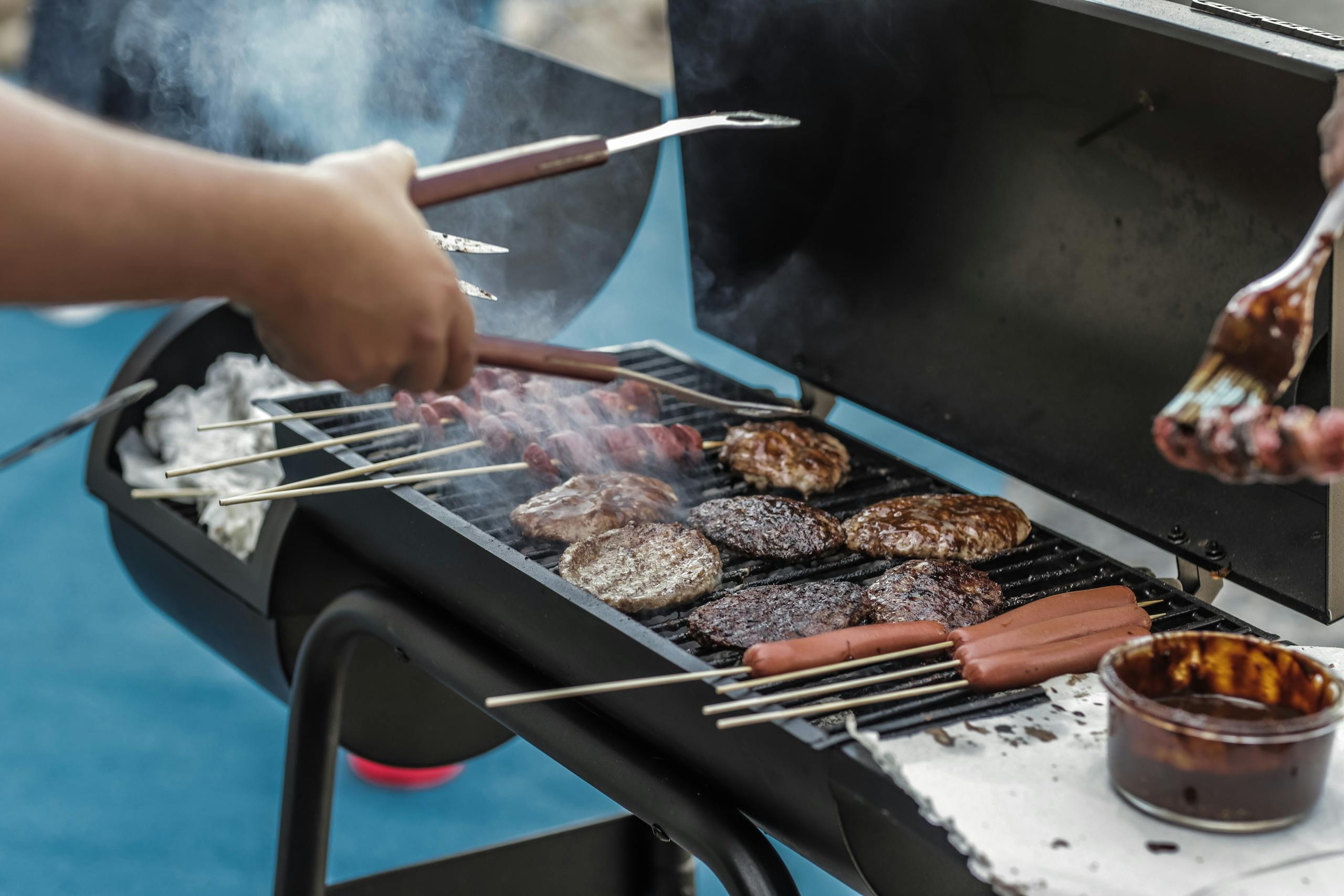 Delicious meats and sausages grilling on a barbecue outside, perfect for a summer picnic.