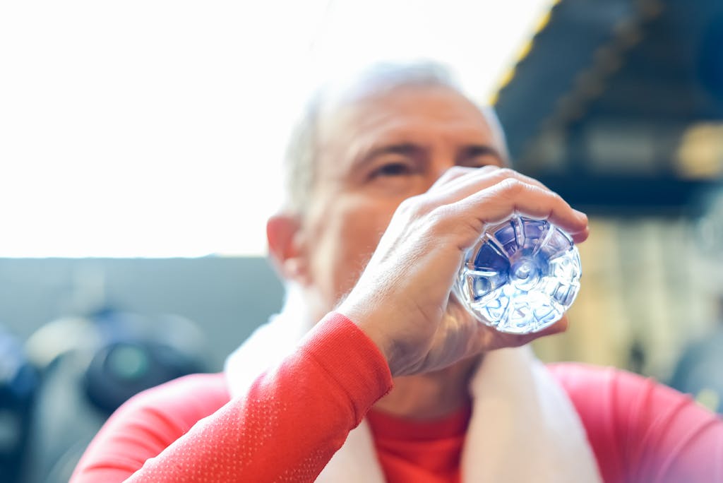 Avoid These 8 Heat Wave Mistakes Before They Harm Your Health 3 Elderly man in red shirt sipping water during gym session.