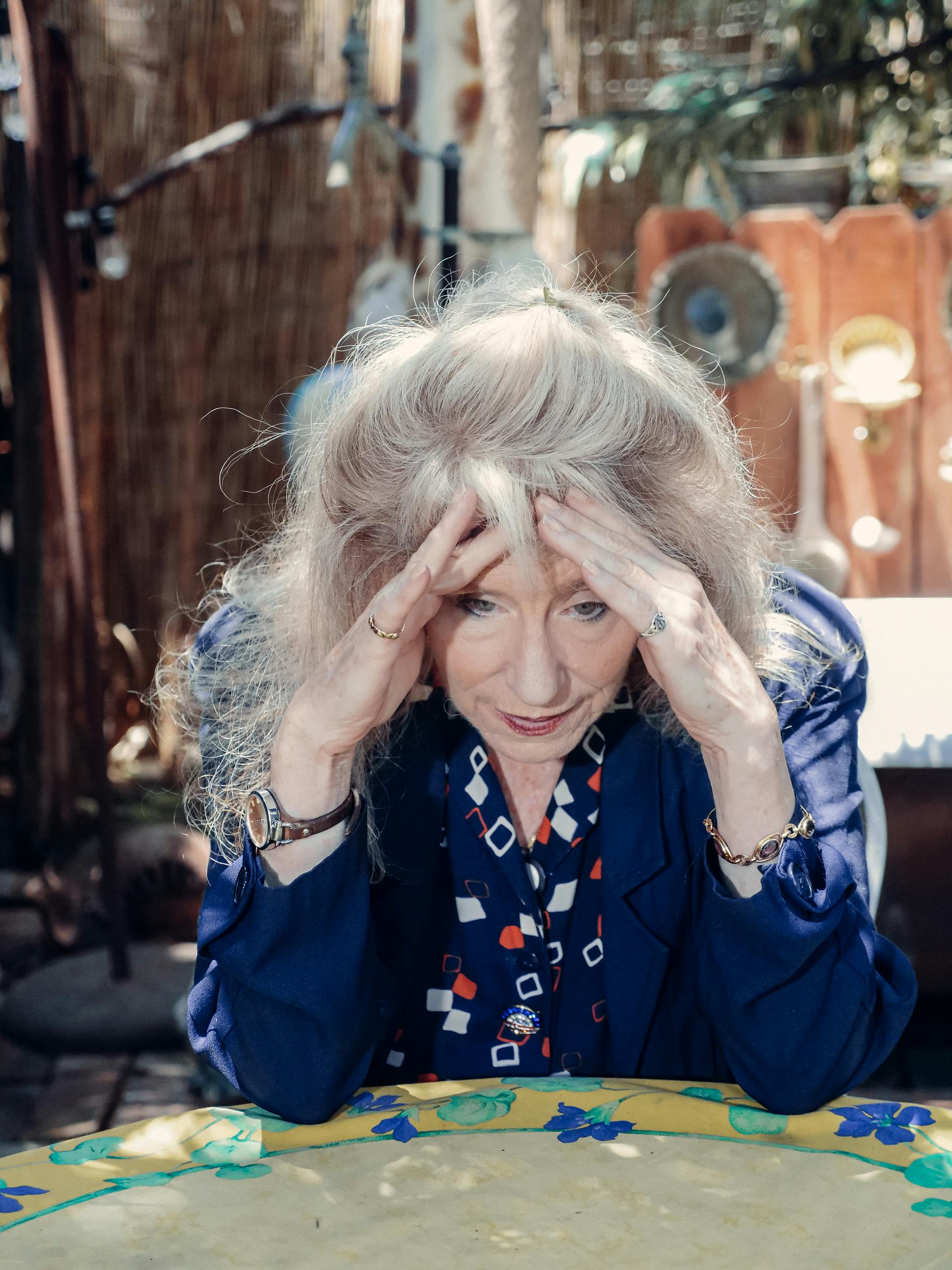 Elderly woman seated indoors with head in hands, expressing distress and worry.
