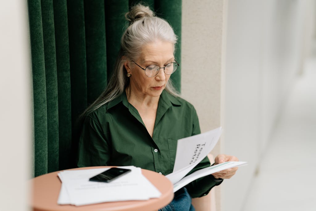 8 Disturbing Signs You’ve Already Hit 50, Whether You Like It or Not 3 Elderly woman with gray hair reading papers at a small table indoors, focused and thoughtful.
