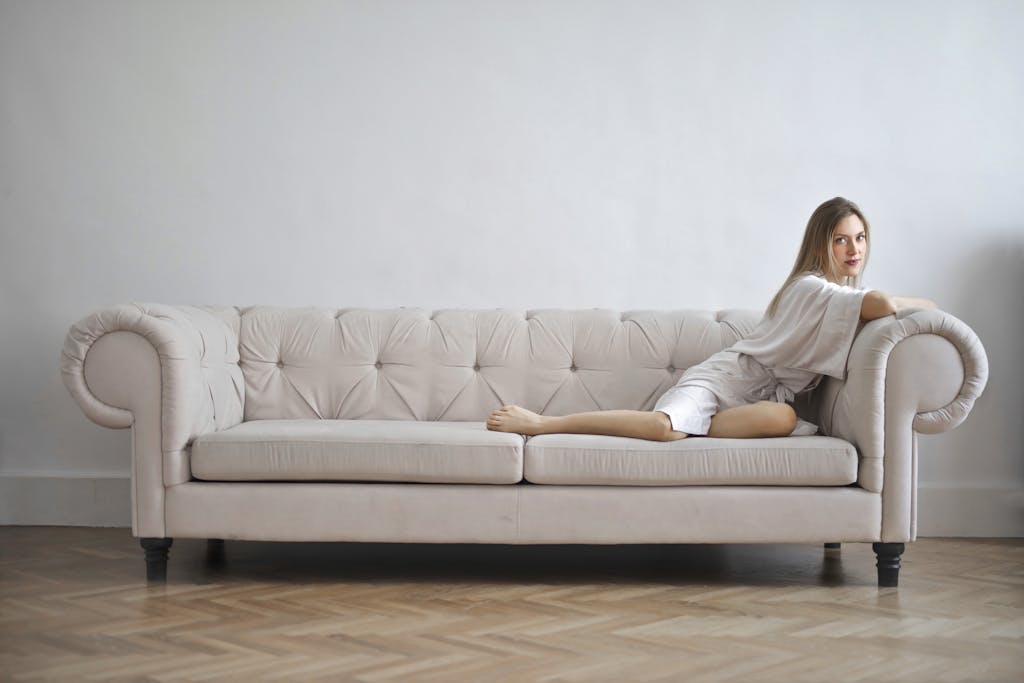 Elegant woman in silk robe reclining on a white sofa indoors, exuding calm and sophistication.