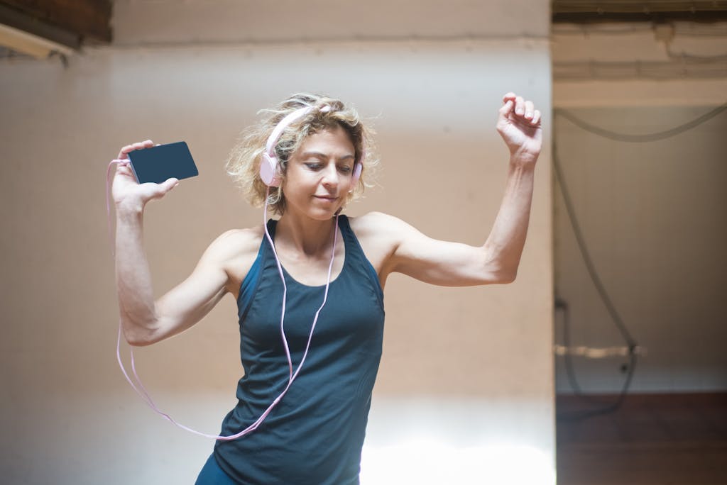 Energetic woman with headphones dancing indoors, enjoying music on her smartphone.