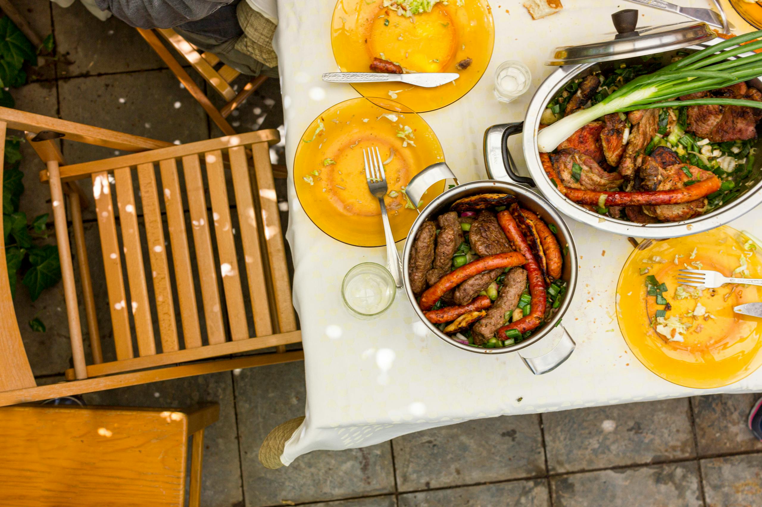 Enjoy a hearty outdoor meal featuring various grilled meats served on a set table in a garden setting.