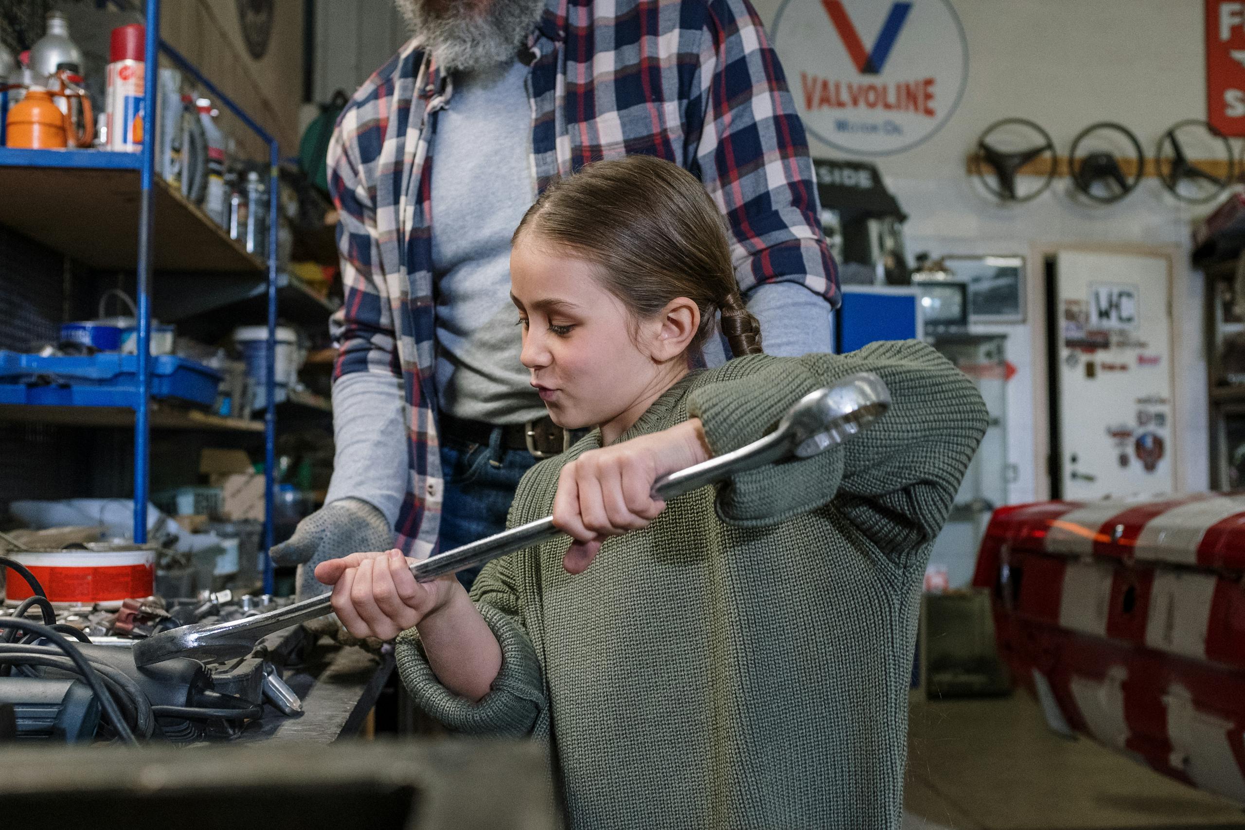 Father and daughter bond while fixing a car in a workshop.