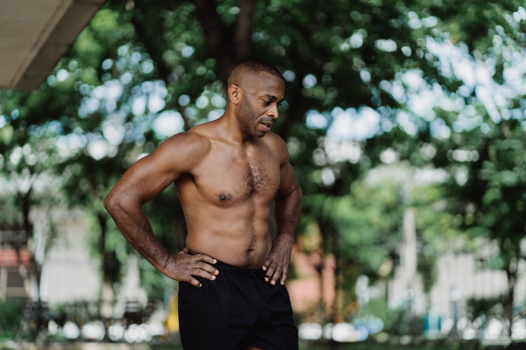 Fit African American man shirtless and exercising outdoors during summer.