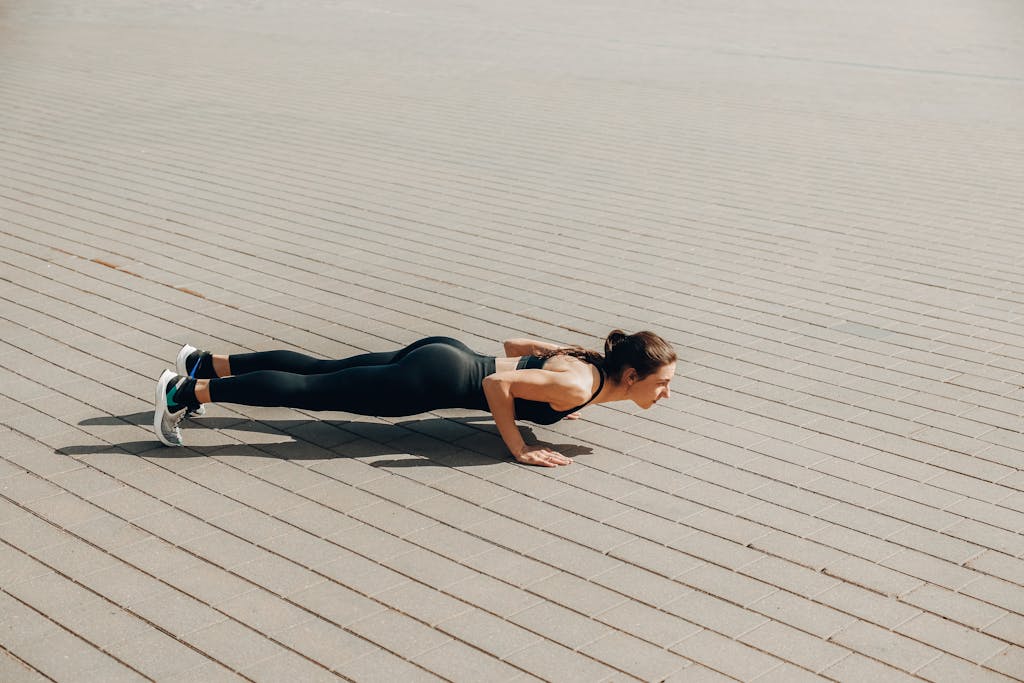Fit woman in activewear performing push-ups outdoors on a sunny day.