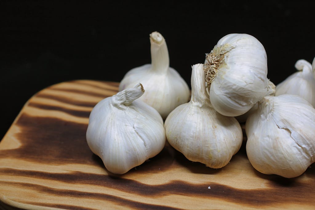 Stop Feeding Your Dog These 12 Dangerous Foods 4 Fresh garlic bulbs placed on a wooden board with a black background, perfect for culinary themes.