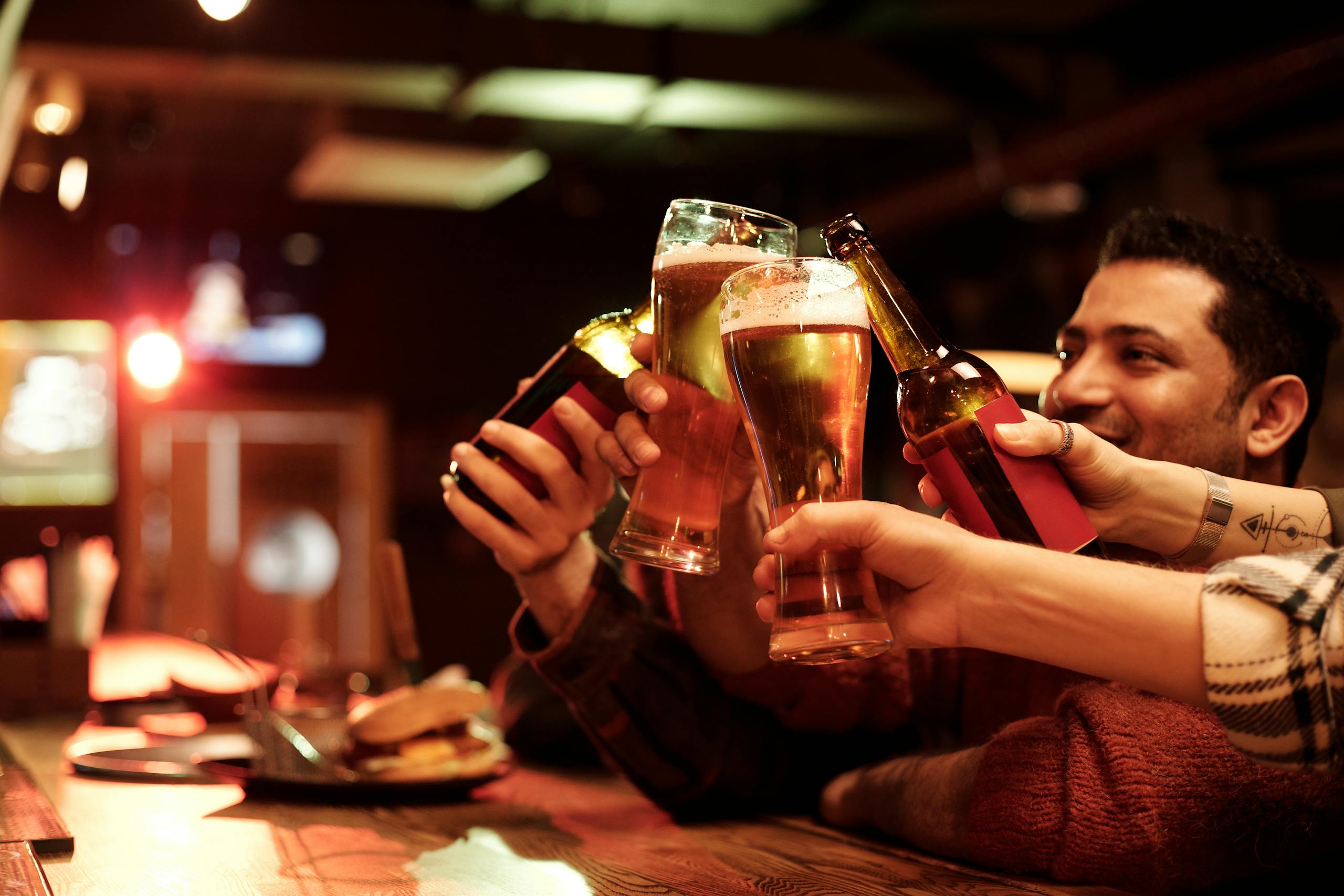 Friends celebrating and toasting with beers in a warm and cozy bar environment for joy and friendship.