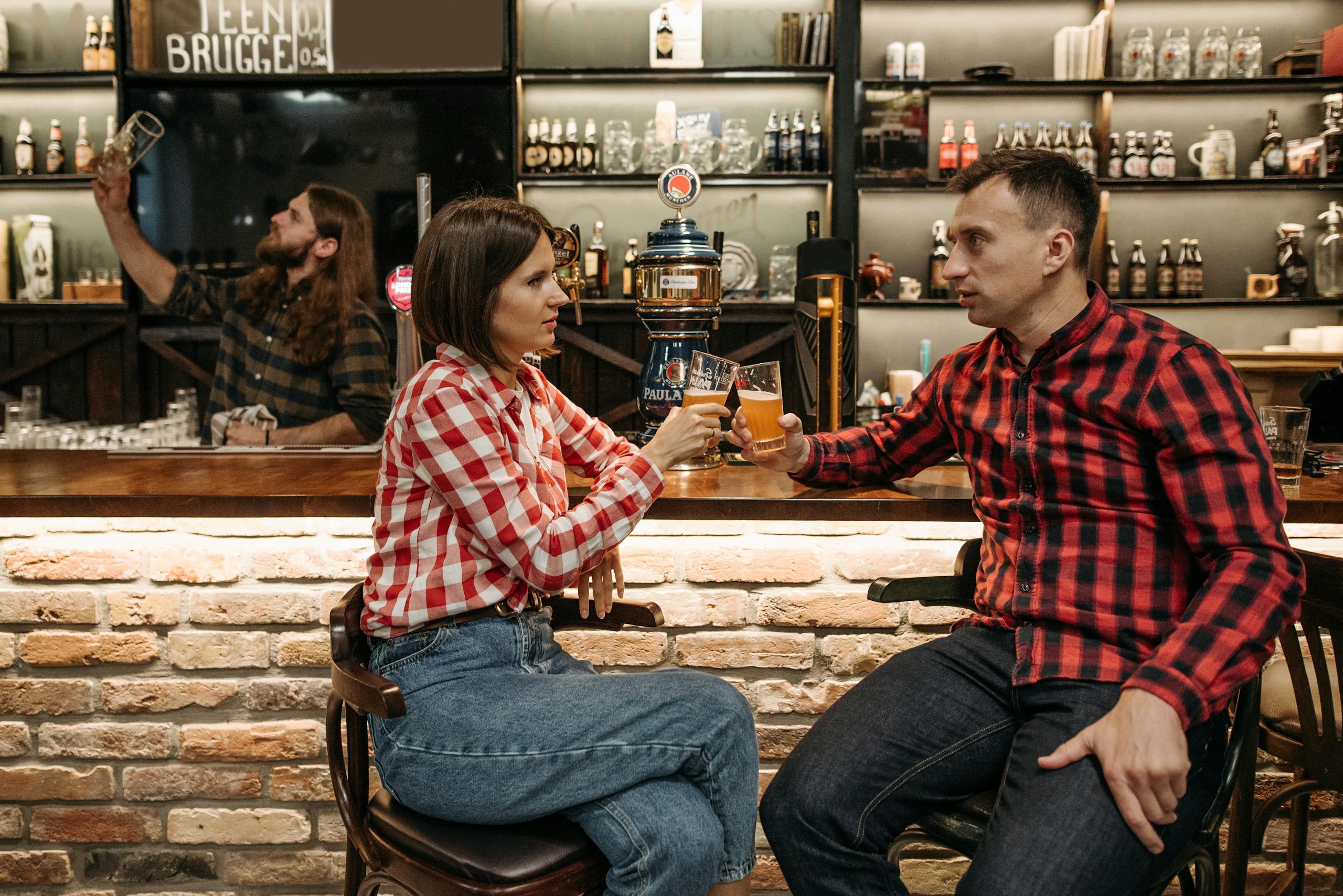 Friends enjoying drinks and conversation in a cozy bar setting, wearing checkered shirts.