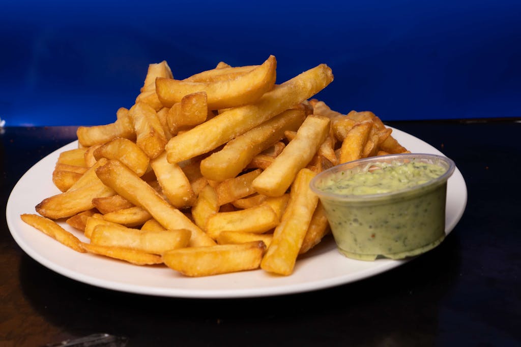 Golden crispy french fries served with a rich avocado dip on a white plate.