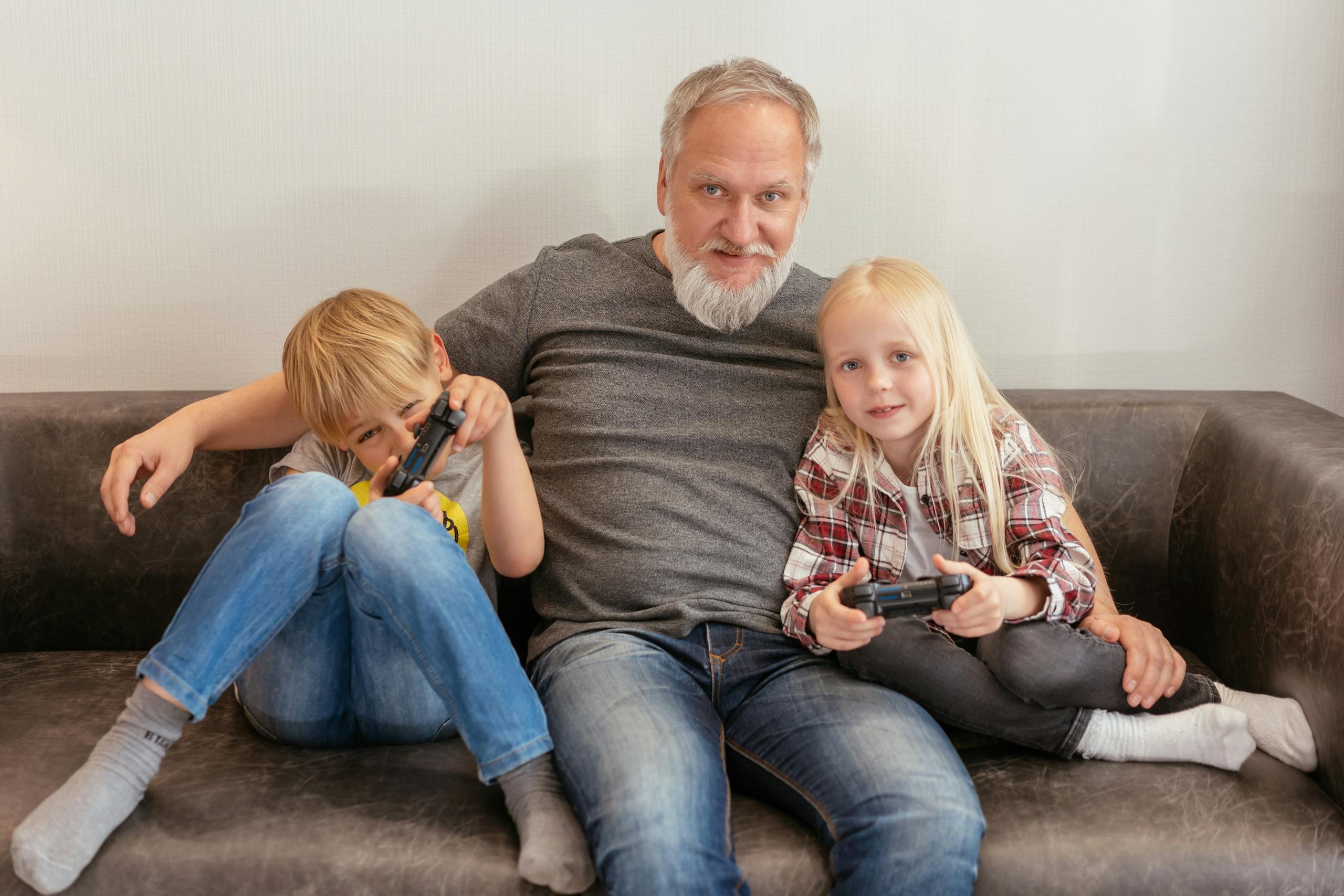 Grandfather and grandchildren enjoying video games together, embracing family fun.