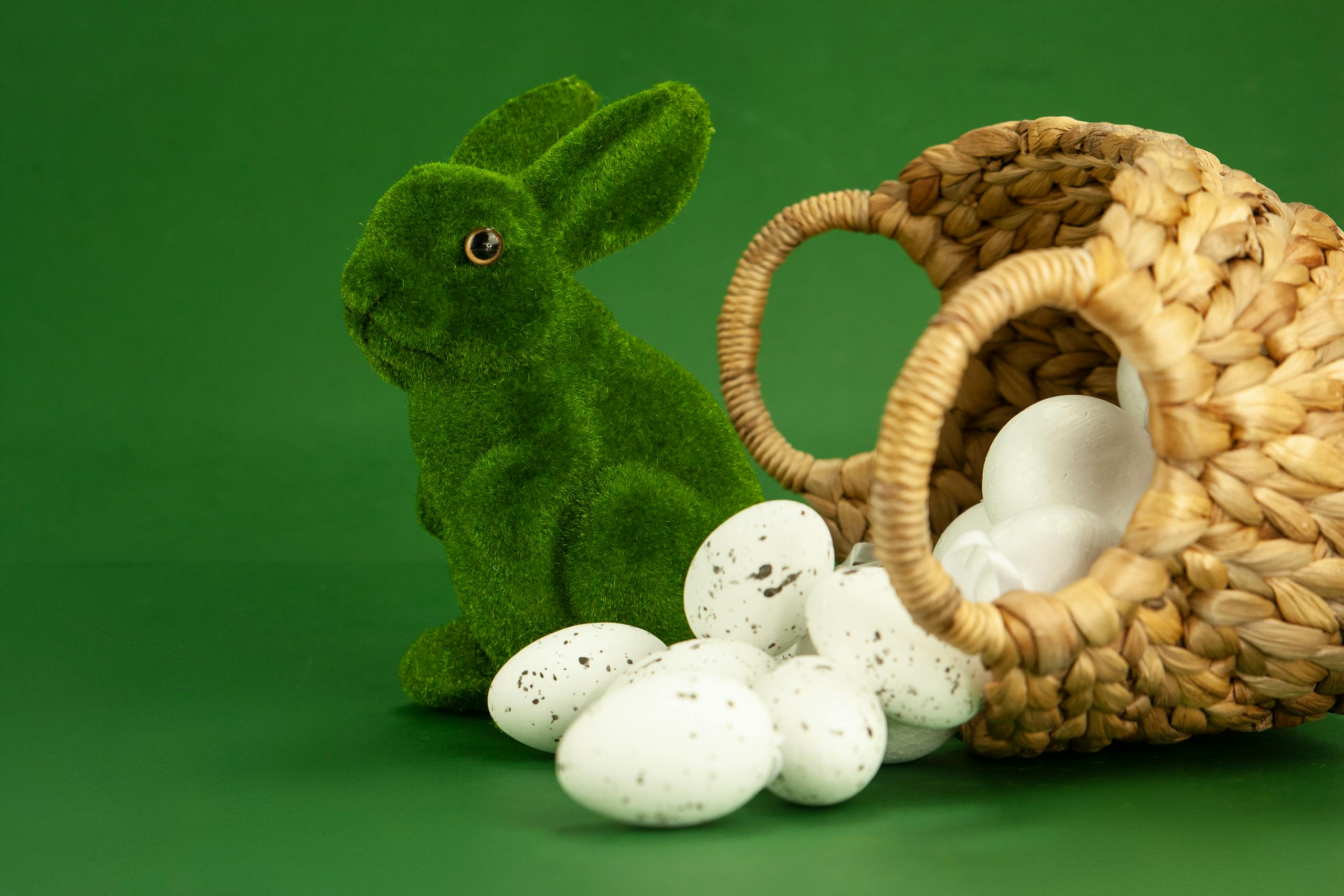 Green bunny figurine with quail eggs and woven basket on a green background.