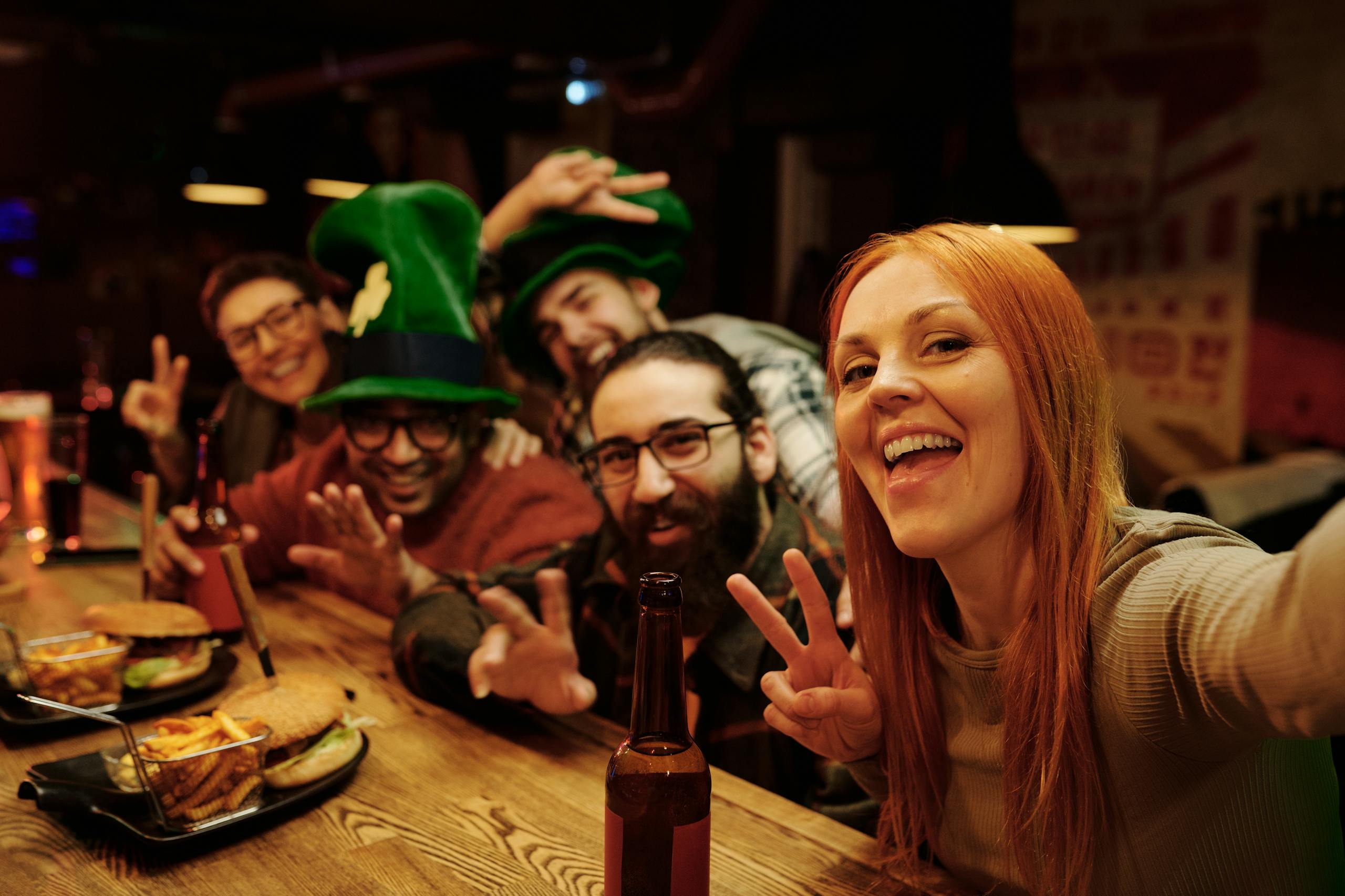 Group of friends enjoying St. Patrick's Day celebration at a bar with festive hats and drinks.