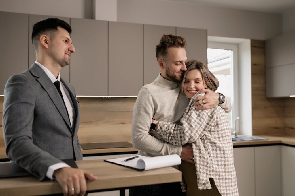 Happy couple embracing in their new home with a real estate agent present.