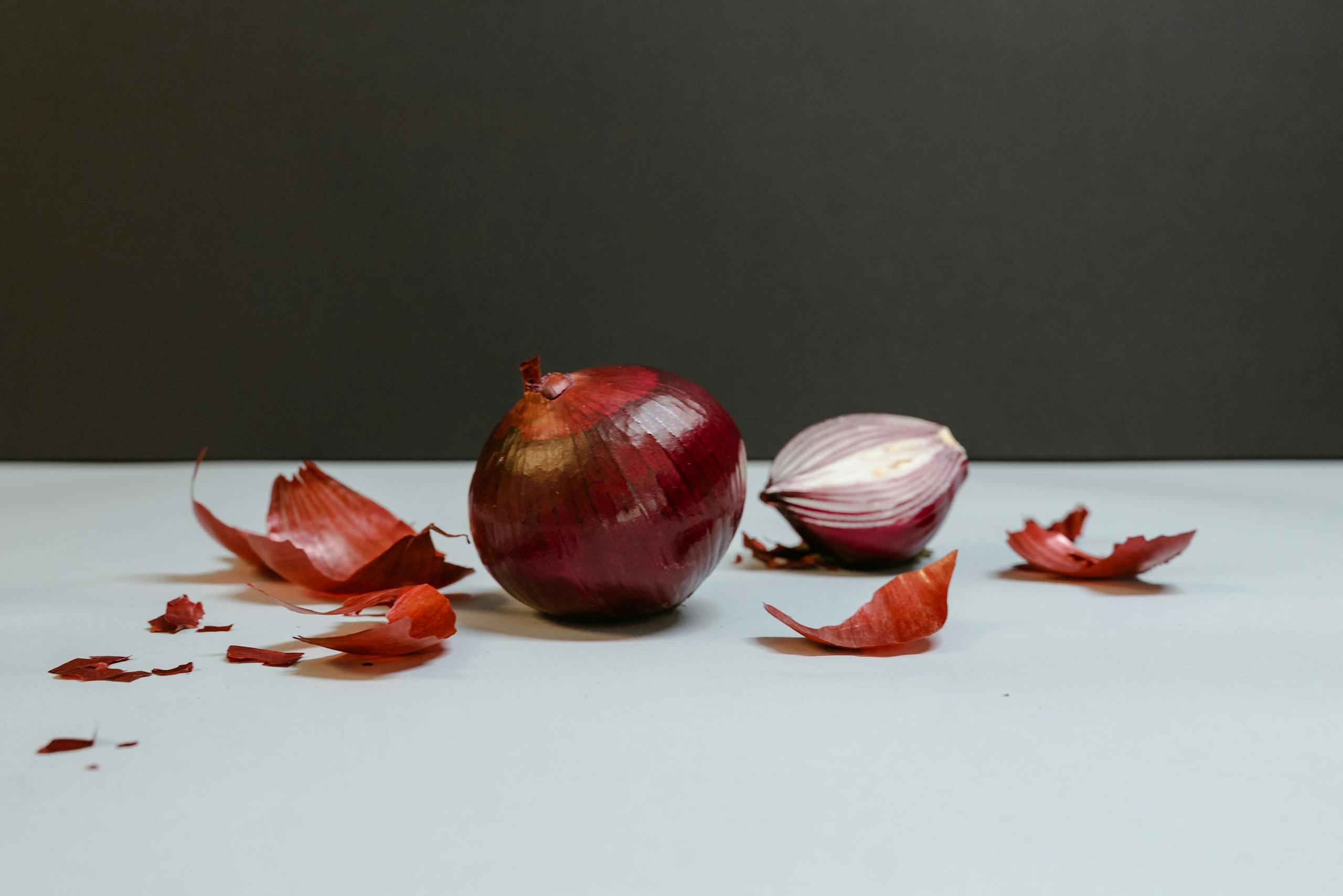 Image of red onions with scattered peels on a white table against a dark backdrop.