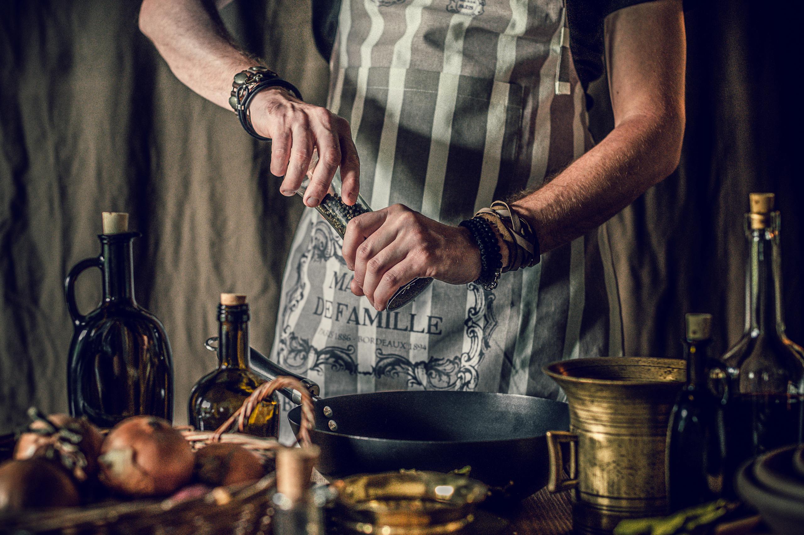 Male chef seasoning ingredients in a rustic kitchen setting. Perfect for culinary themes.
