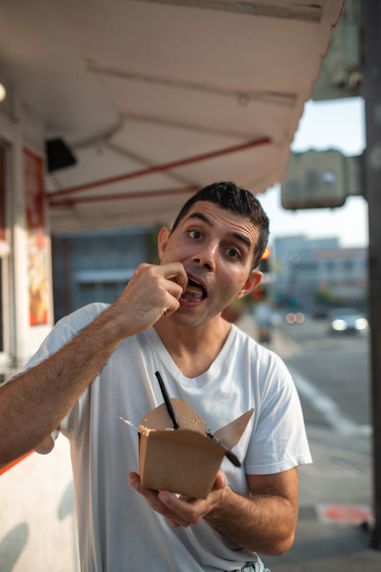 Man enjoying street food from a takeout box on a sunny day outdoors.