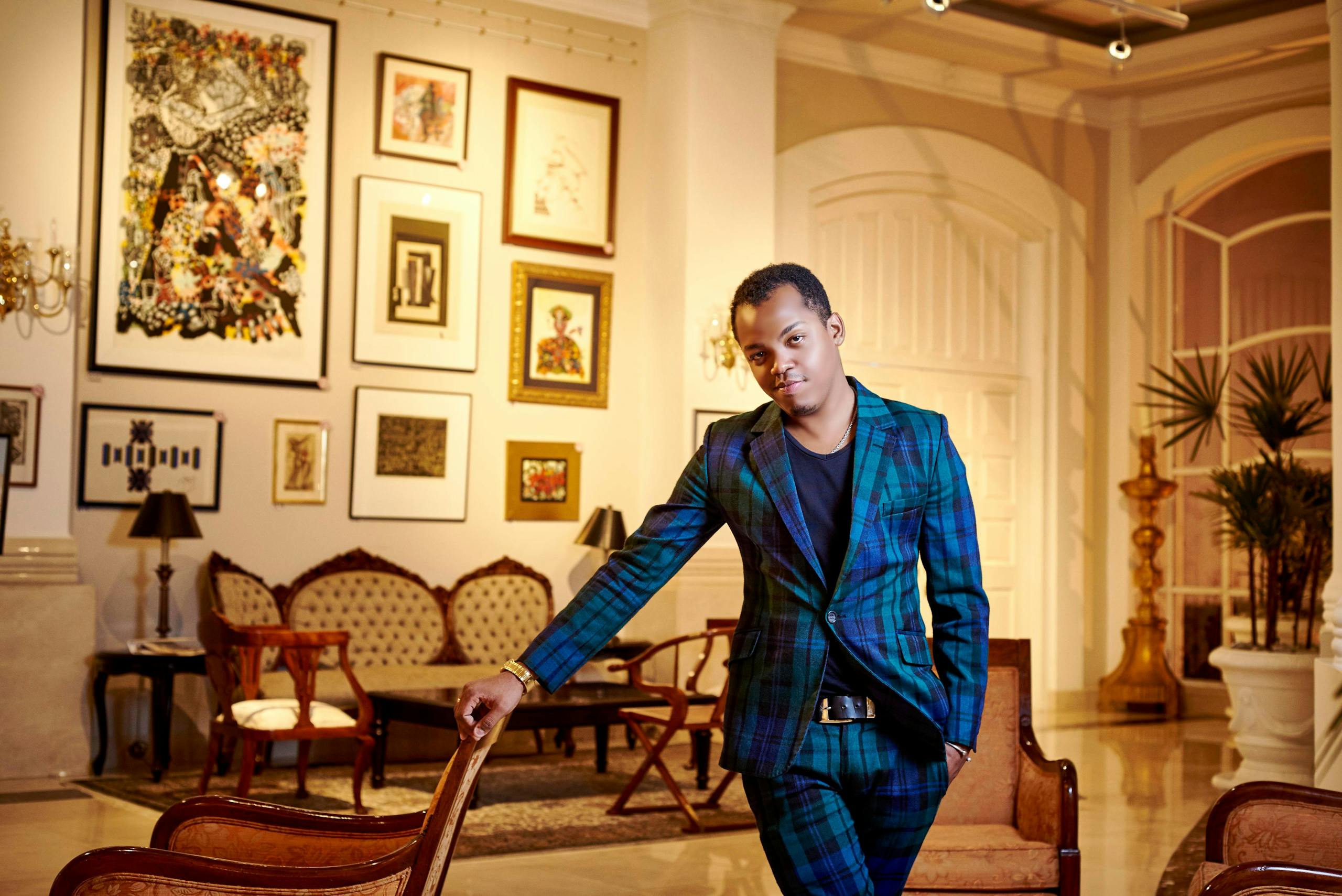 Man in a stylish suit leaning in a luxurious, art-filled living room interior.