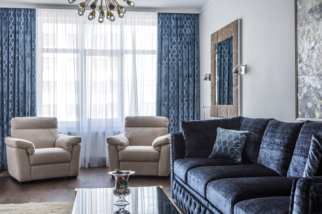 Modern living room with blue sofa, beige armchairs, and chic chandelier.