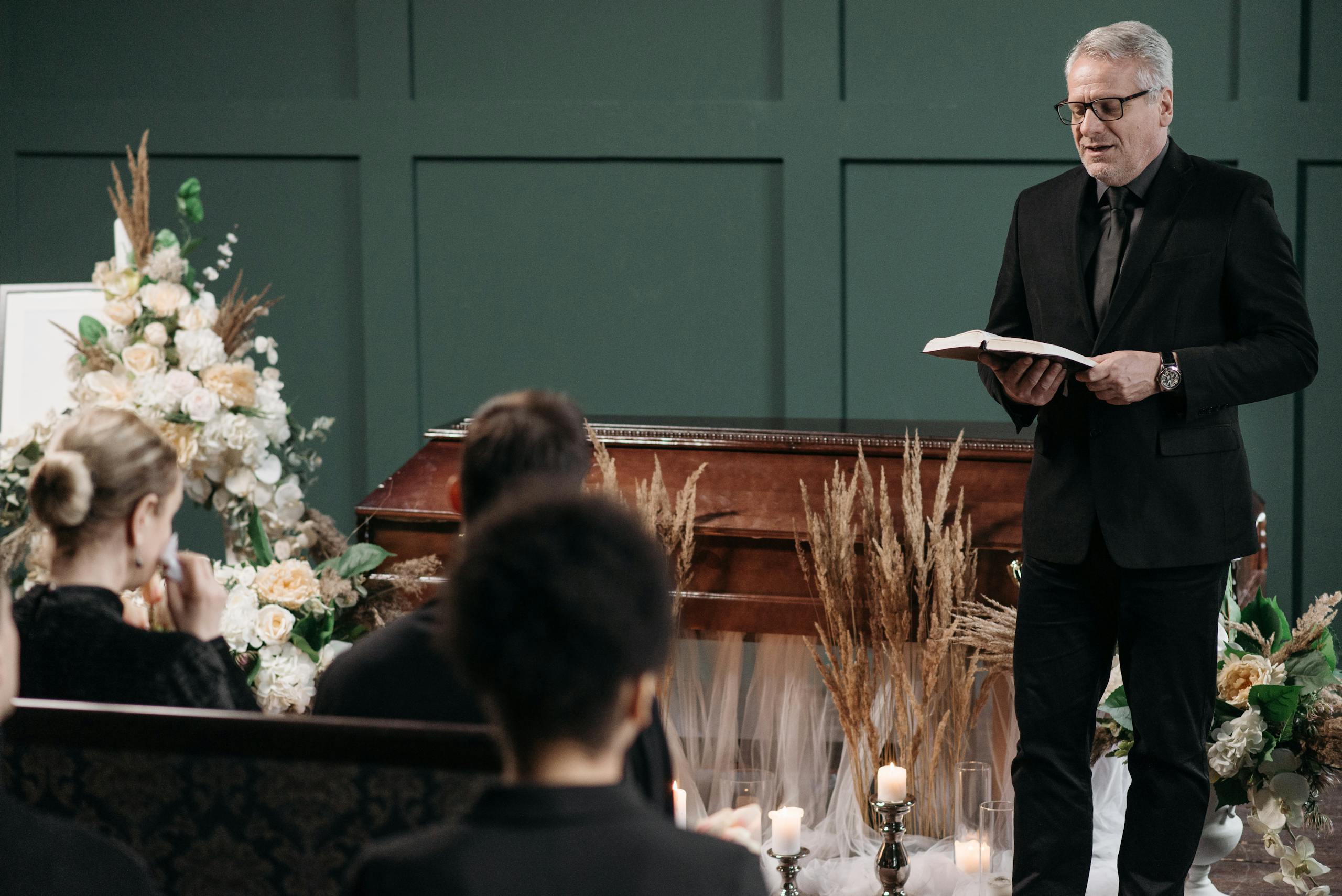 Pastor leading a funeral service with a coffin and floral arrangements.